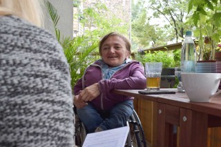 Rebecca Maskos sitzt in ihrem Rollstuhl am Balkontisch vor einem Glas Tee.